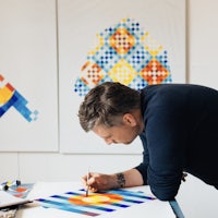 a man is painting on a table in front of colorful paintings